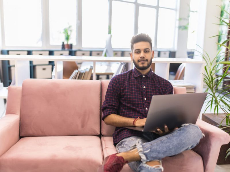 Casual young man using laptop with happy on sofa in modern office, process color.