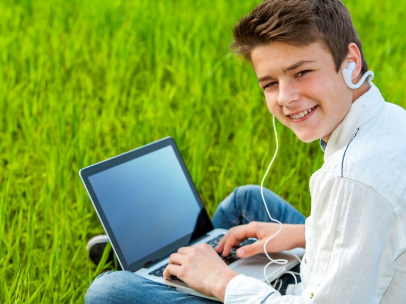 Close up portrait of teen student working on laptop in green grass field.
